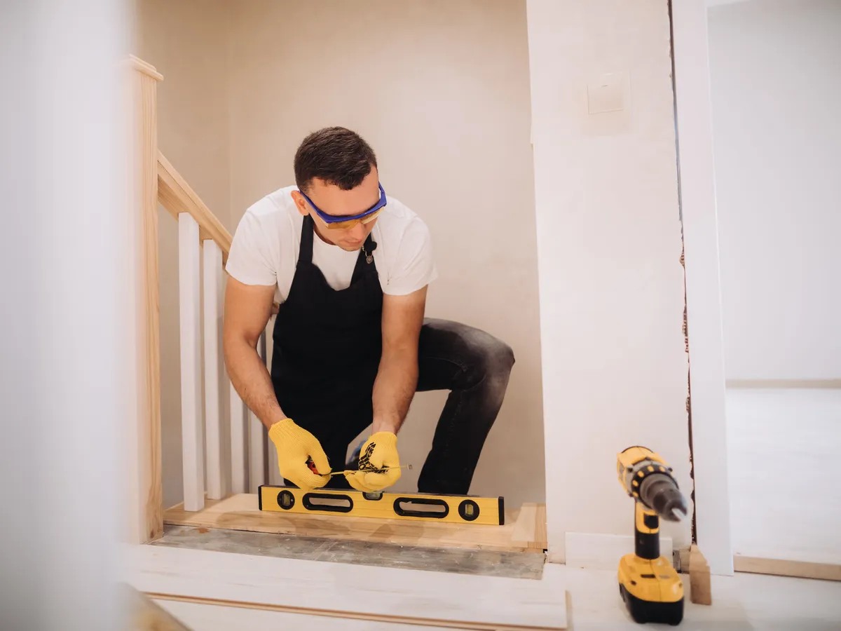 Craftsman in safety glasses checking a new stair tread with a spirit level