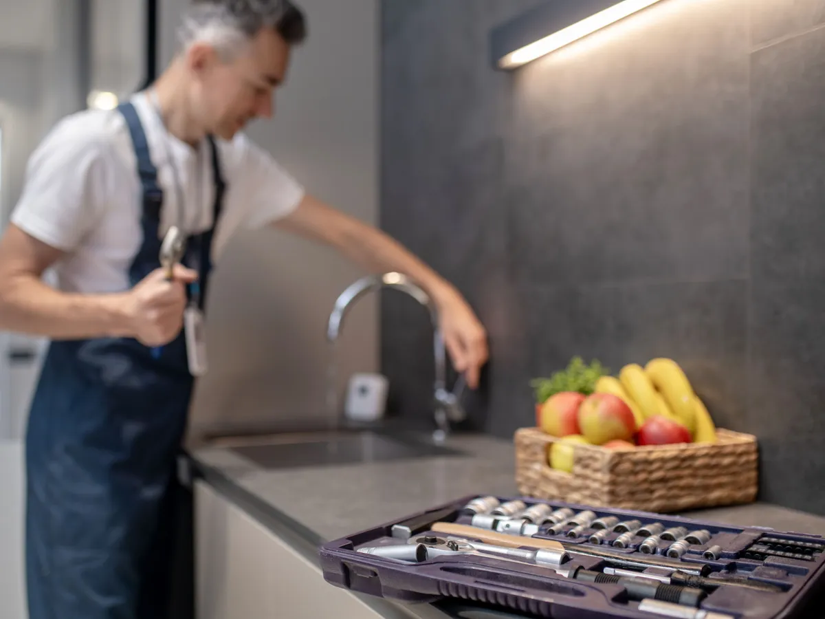 Handyman with a wrench at a kitchen sink, an open socket set on the counter