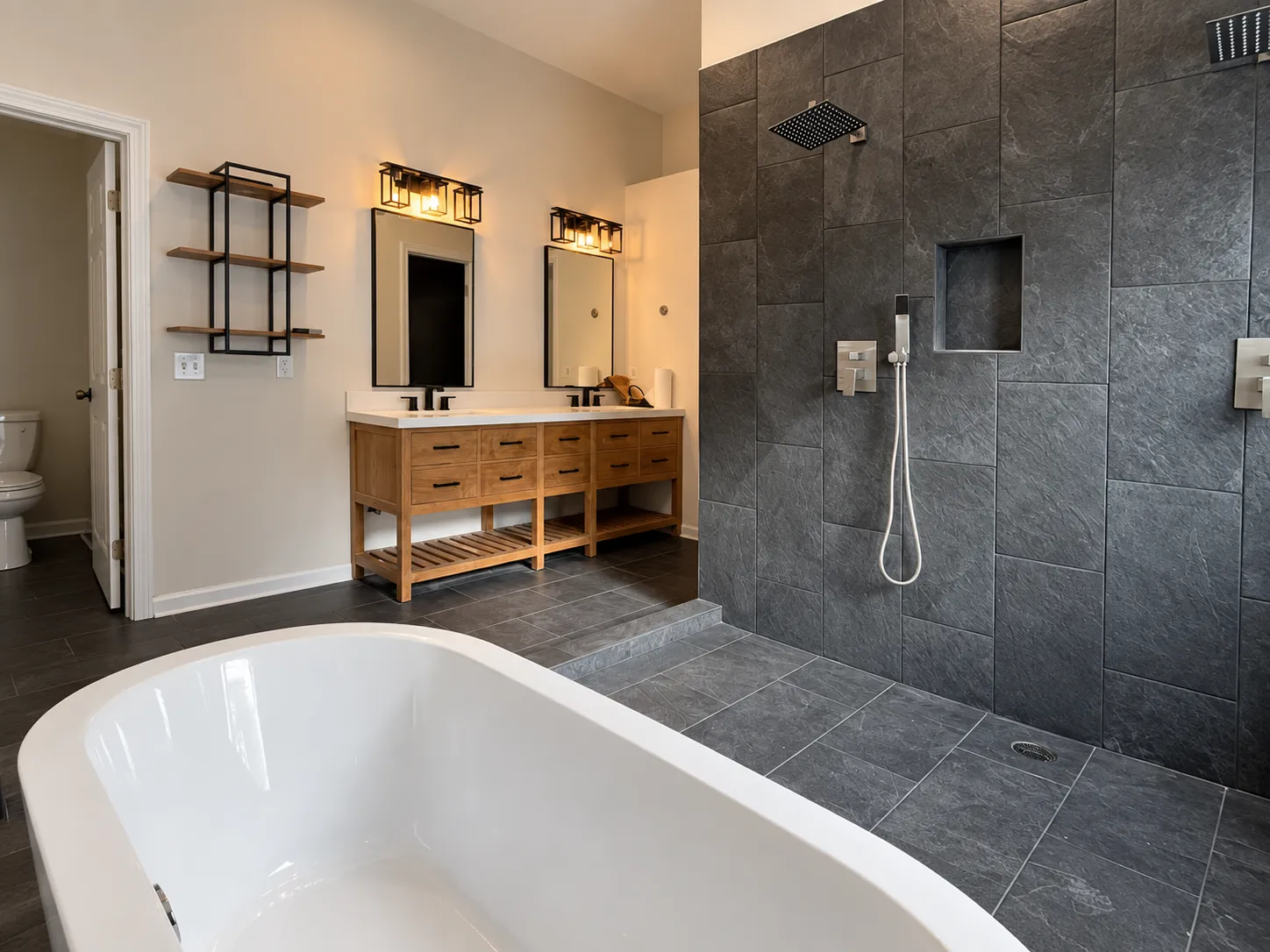 Renovated bathroom with a dark slate-look tiled walk-in shower, a white freestanding tub and a double wood vanity