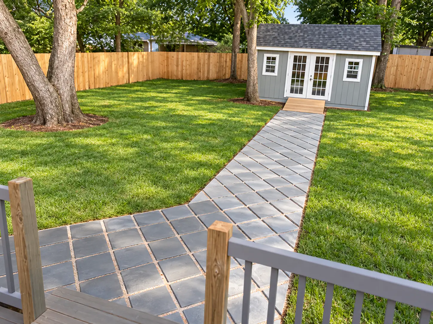 Design concept of the same backyard, with a grey paver walkway leading from the deck to a grey garden shed with French doors