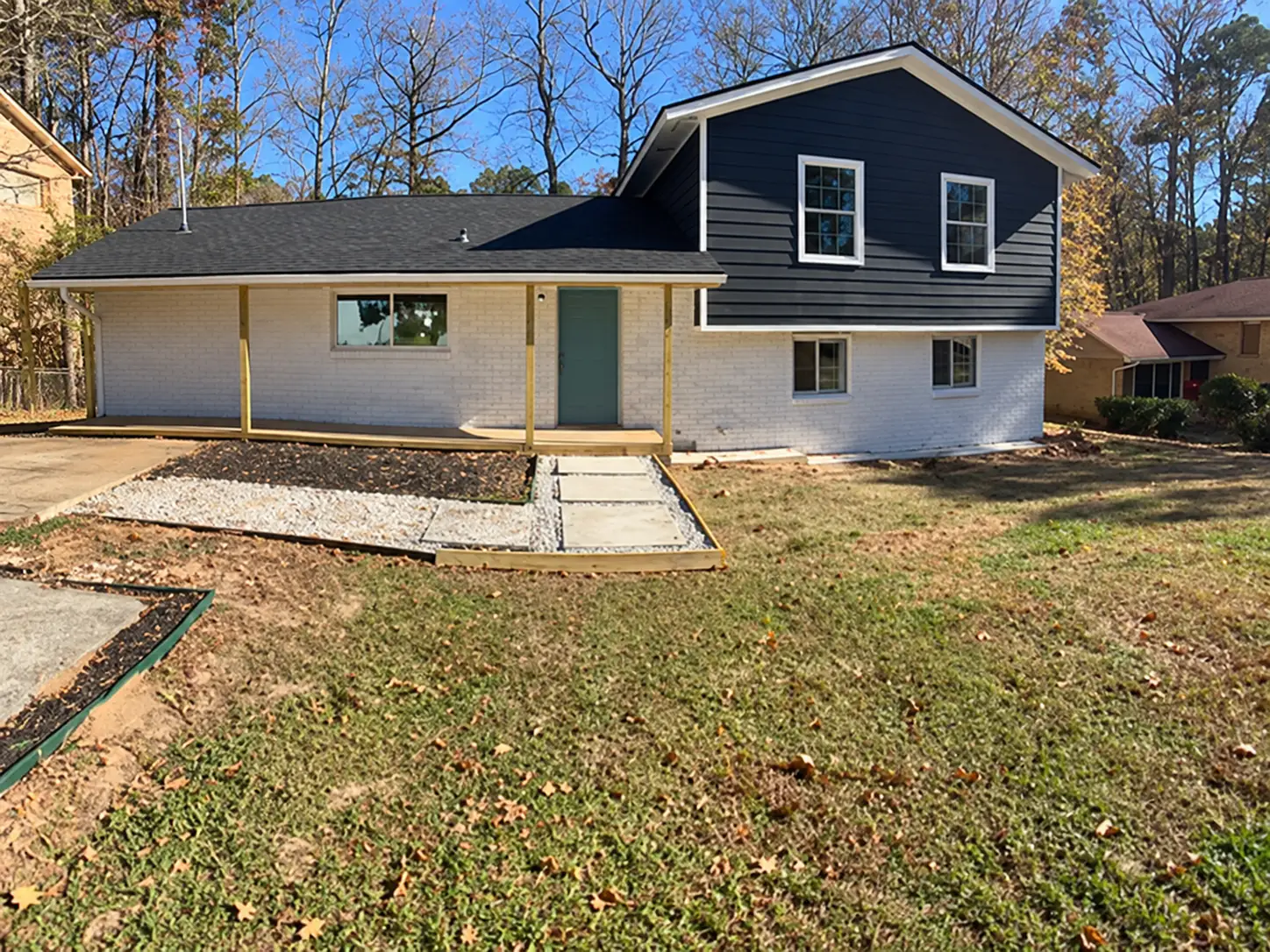 Split-level house with white painted brick, navy siding, an unfinished wood porch frame, a gravel and stepping-stone path and a patchy lawn