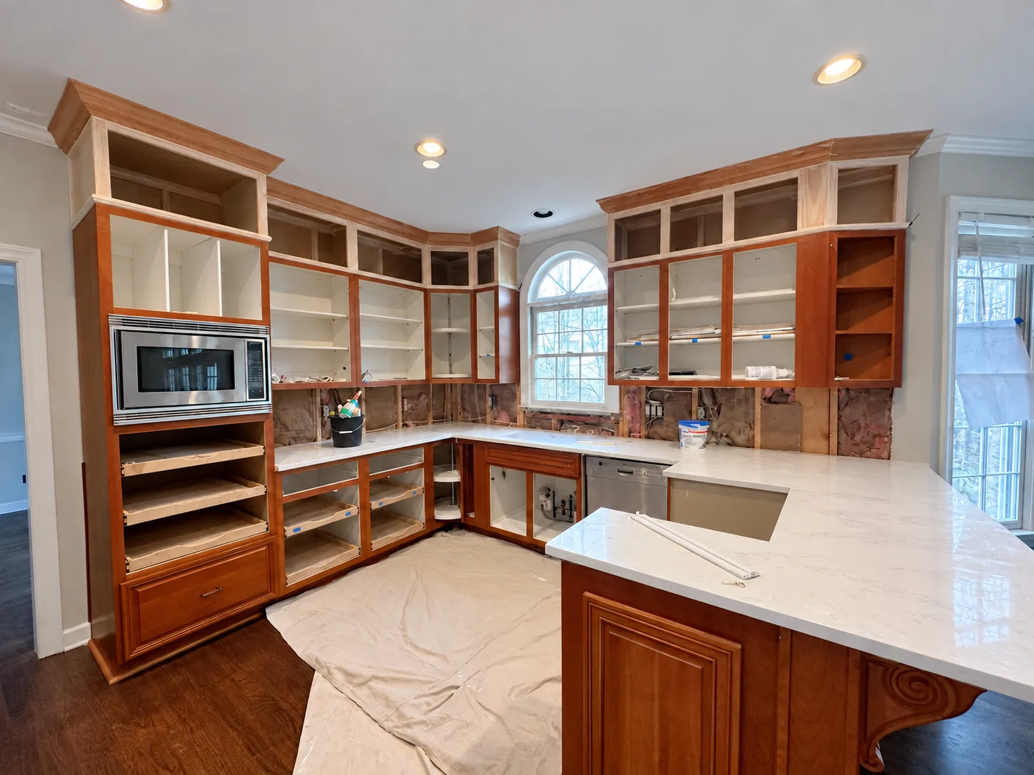 Kitchen mid-renovation, with cherry cabinets stripped of their doors, open stud walls and new white quartz countertops