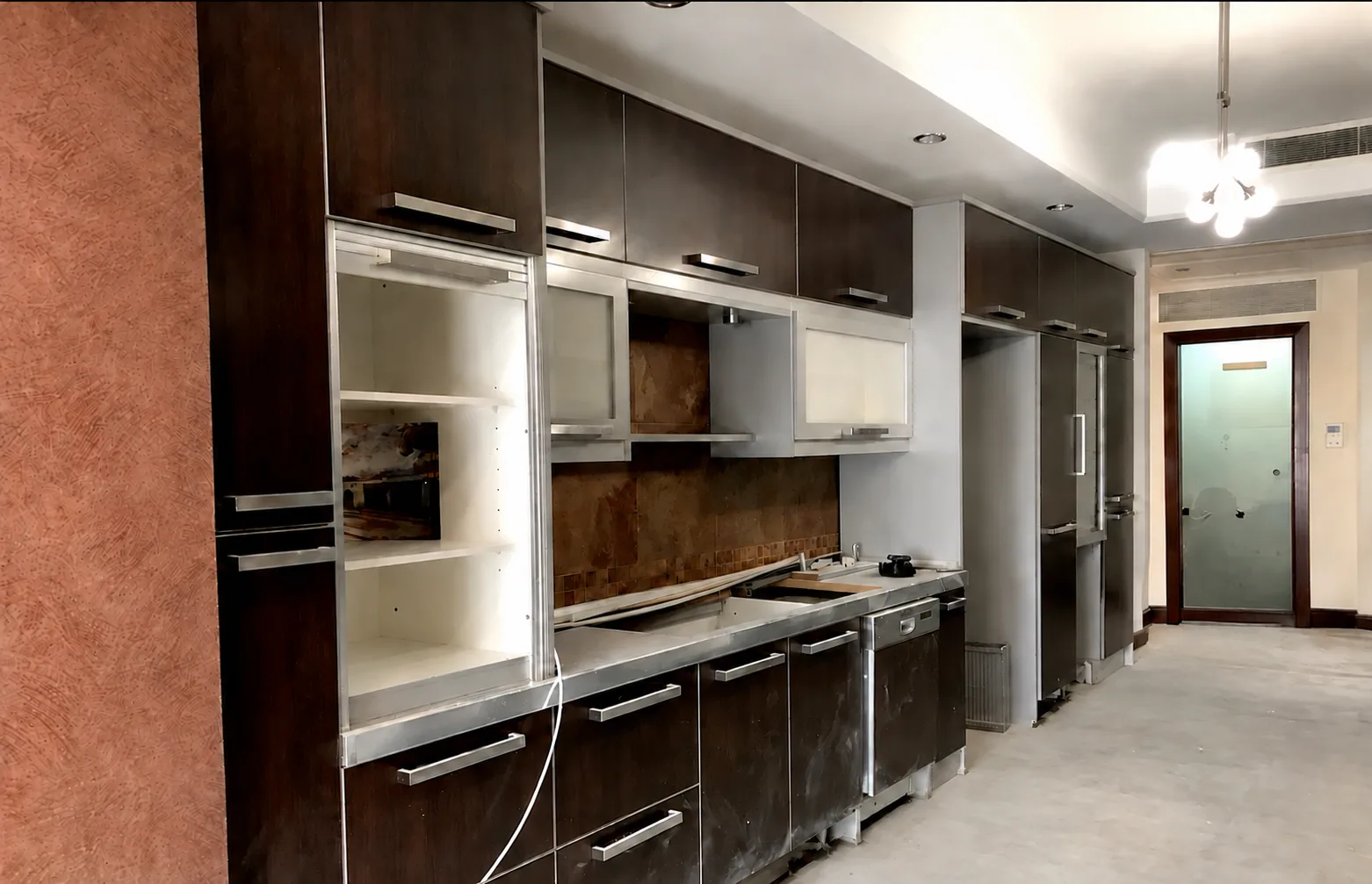 Galley kitchen before renovation, with dark wenge slab cabinets, aluminium-framed glass doors, a stainless countertop and slate tile backsplash