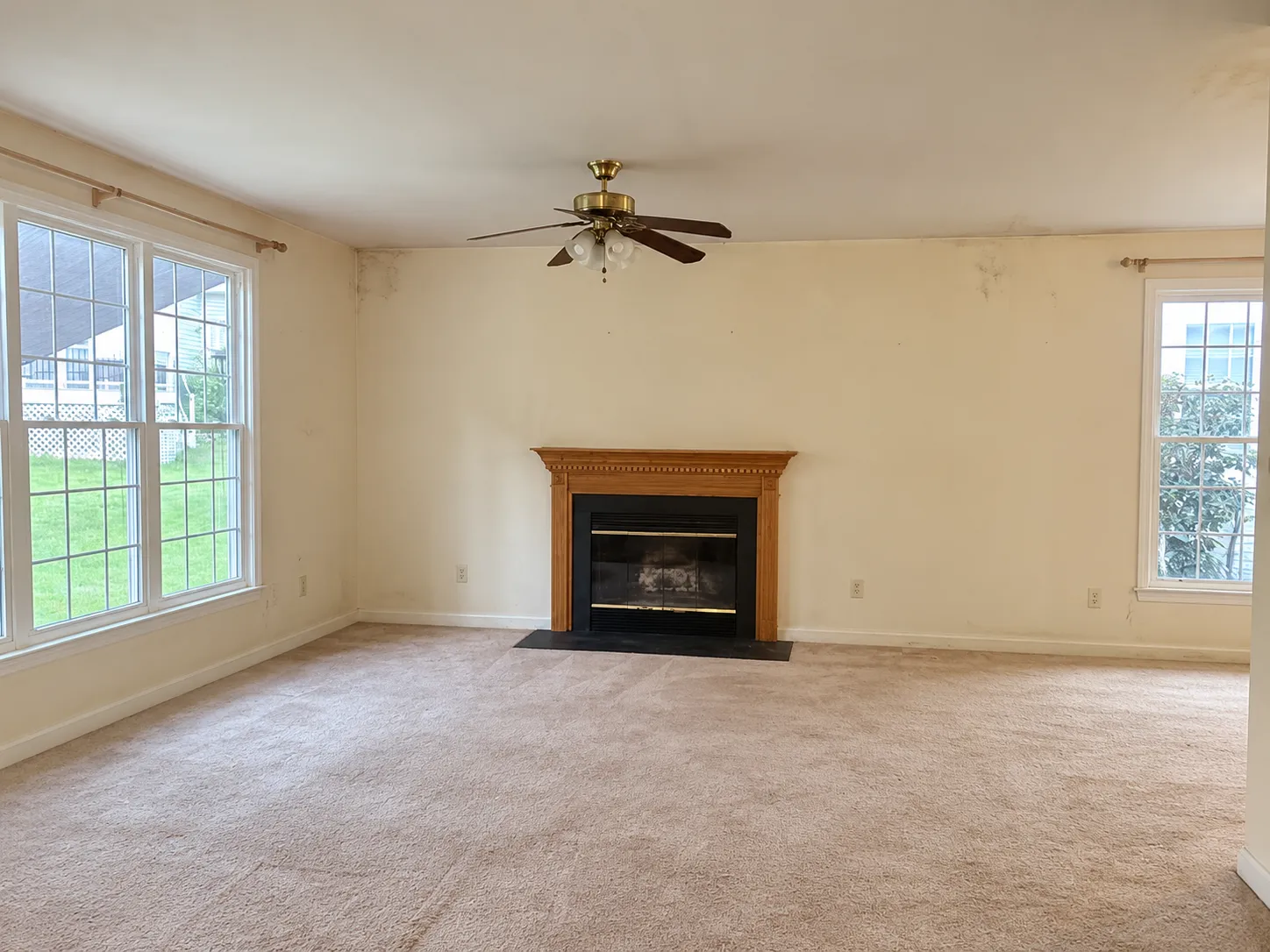 Family room before renovation, with stained walls, beige carpet, a ceiling fan and a fireplace with an oak mantel